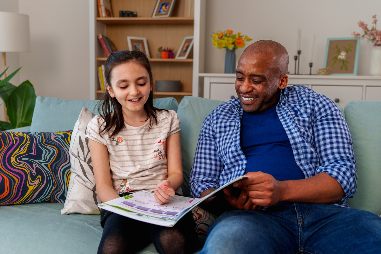 foster parent helping foster child with homework on living room couch